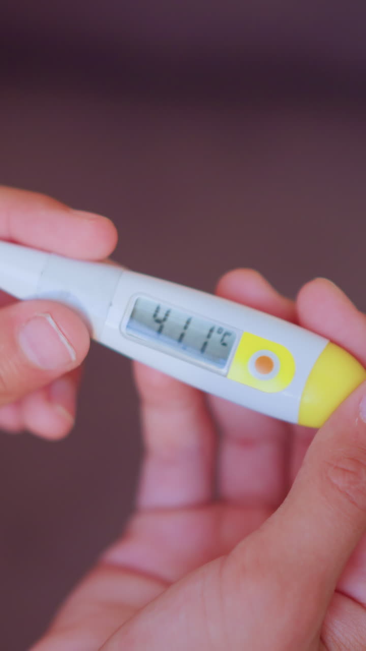 Close up of hands holding digital thermometer displaying high temperature of 41.1 degrees Celsius indicating fever or health emergency with focus on reading