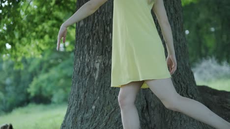 woman in yellow dress dancing by tree in summer park