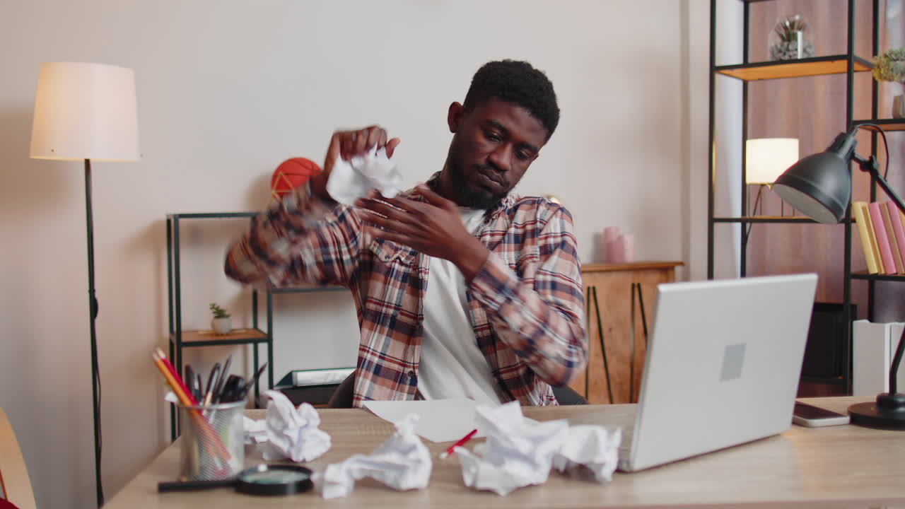 Sad young man working at home office crumples throwing heets of paper with bad ideas and mistakes