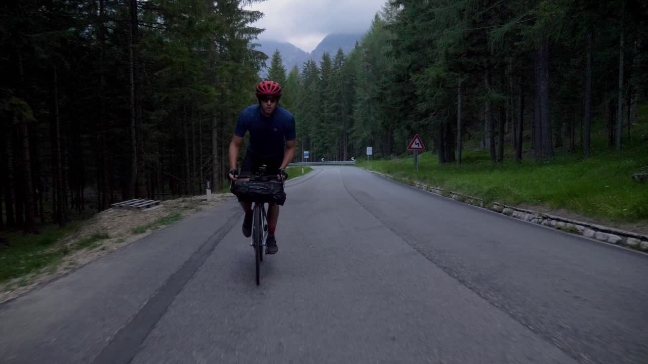 Man in sporty outfit cycles through the forest at a high speed on an early morning in the Italian mountains, Dolomiti