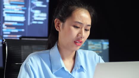 close up of asian female programmer stretching while writing code by a laptop using multiple monitors showing database on terminal window desktops in the office