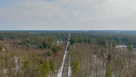 backward drone view flight, tracking a car that is driving on a road of a wintry forest