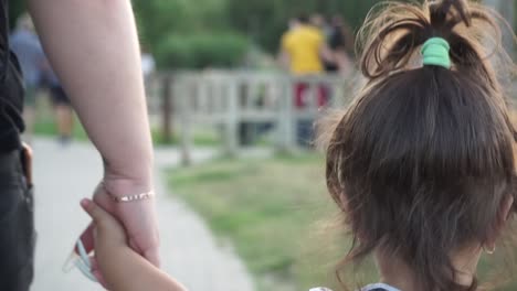 close up behind mother and child holding hands walking through park, slow motion