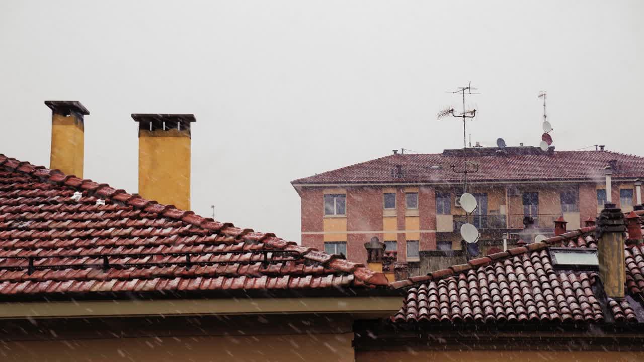 Snowfall on historical italian city seen from rooftop with chimneys