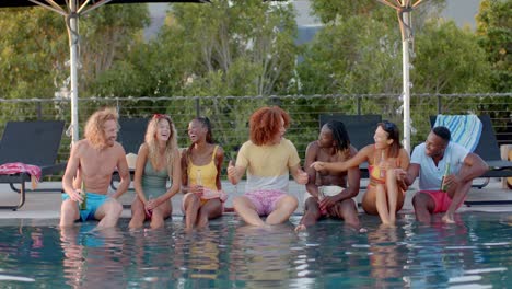 happy diverse friends with drinks talking at pool in slow motion