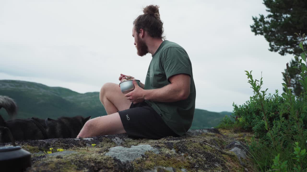 hombre comiendo comida mientras estaba sentado en la roca junto a la orilla del lago