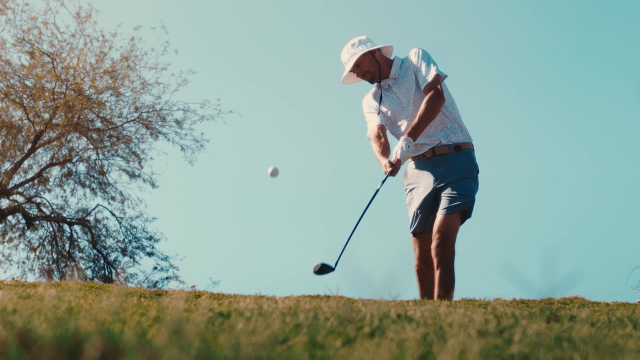 Golfer hits 3 wood over camera in extreme slow motion on sunny summer day wearing bucket hat, 4k 800fps slowmo golf shot low angle pod