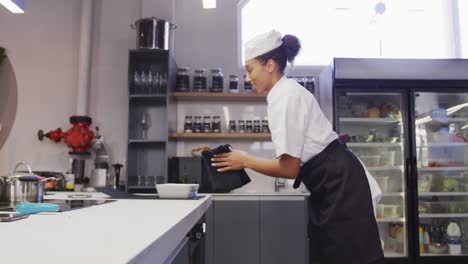 african american female chef wearing chefs whites in a restaurant kitchen,taking food out of an oven