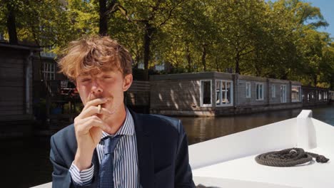 male student with mustache smoking weed on boat in amsterdam canals, gives joint