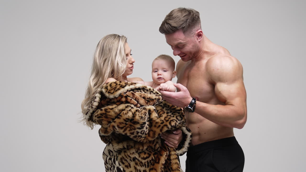 Happy parents having a little baby boy in studio. Man standing near his beloved wife and child. White backdrop.
