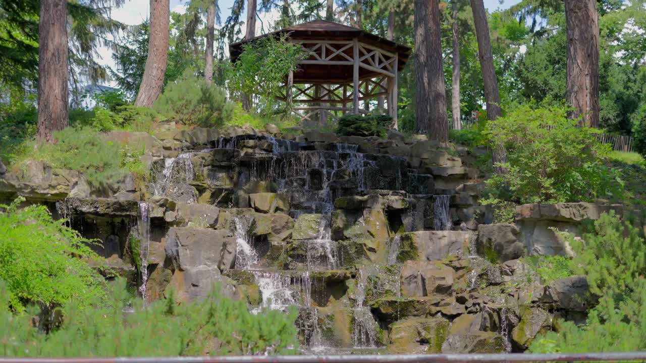 Waterfall in slow motion in T&uuml;rkenschanzpark in Vienna surrounded by trees during a bright sunny day at noon