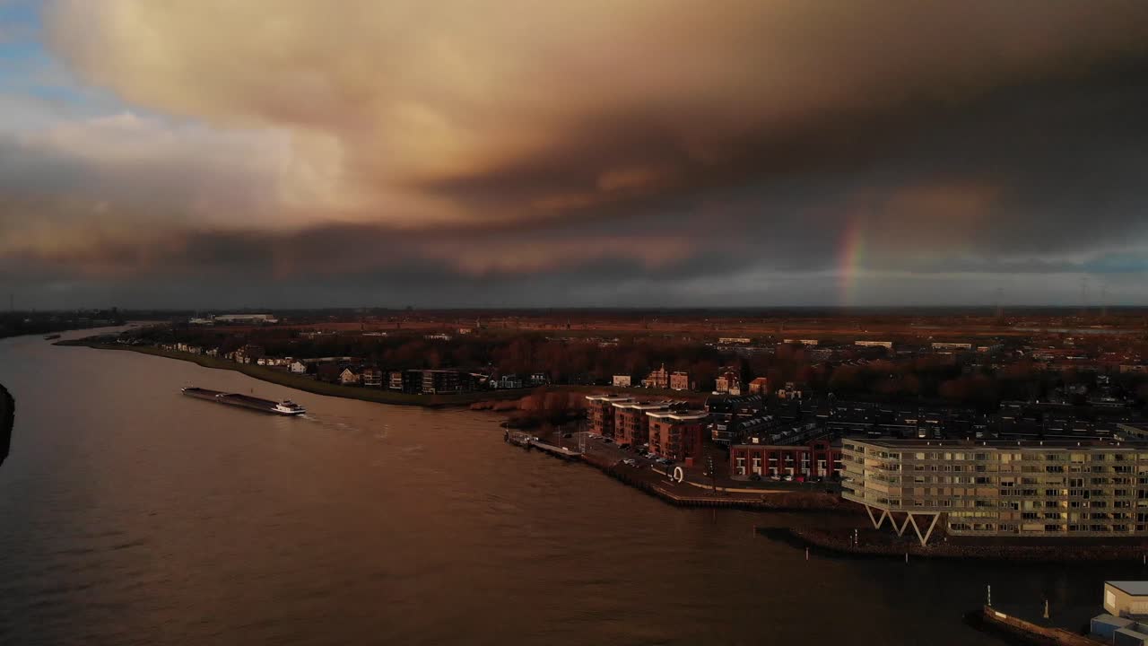 Industrial Barge With Goods Sailing Across Noord River During Sunset With Rainbow In The Distance In Netherlands. - aerial