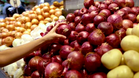 a person selects red onions from a vibrant display in a well-lit gold coast supermarket