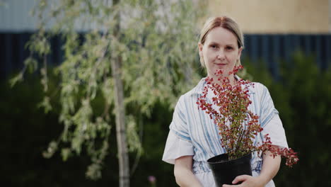 a middle-aged woman holds a pot of barberry. greening your home, working in your garden