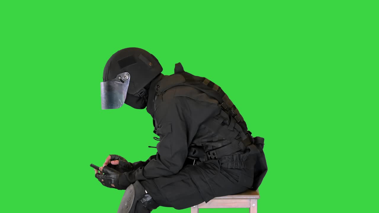Tired riot policeman using smartphone after work on a Green Screen, Chroma Key