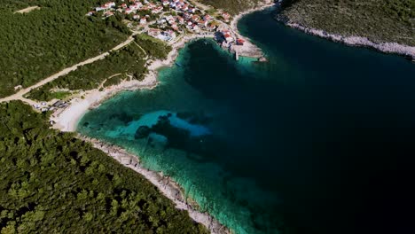 Top-down-view-of-a-tropical-Mediterranean-town-located-on-an-island-beach-with-clean-water