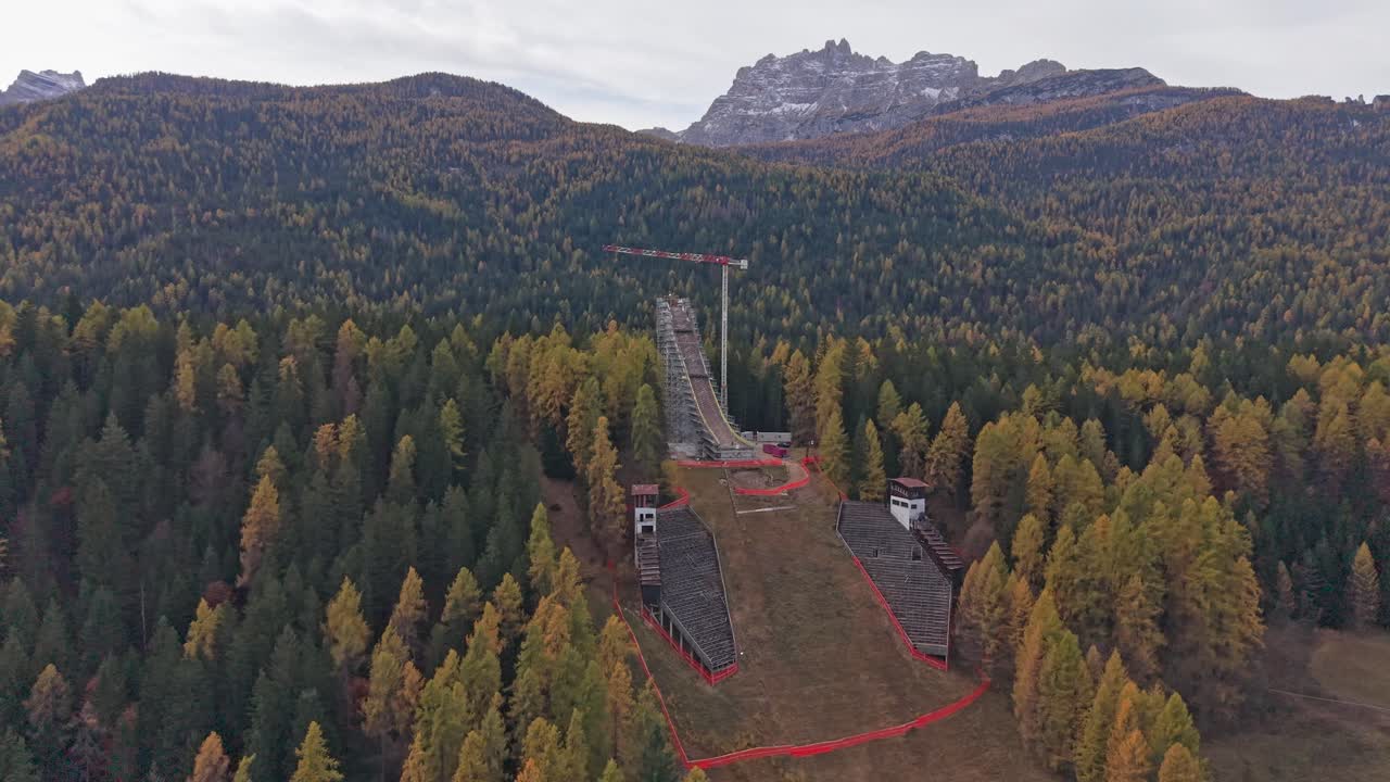 Ripresa aerea panoramica di una gru e operai che costruiscono un trampolino da sci su un ripido pendio.