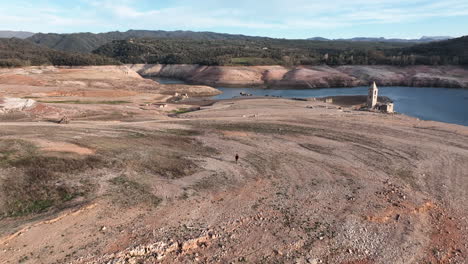 vista panorámica de un hombre caminando en tierra seca cerca del embalse de sau