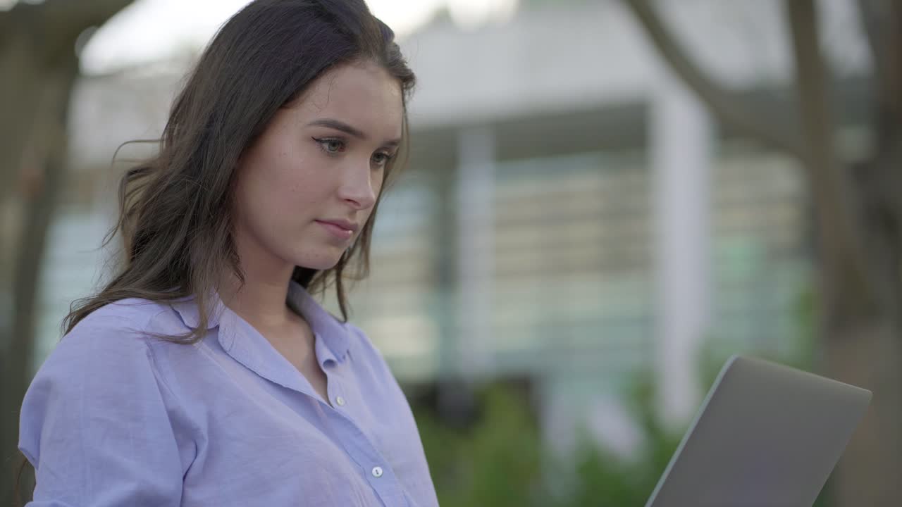 vista lateral de una mujer caucásica bonita en el parque trabajando en una computadora portátil