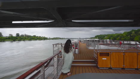 Woman-on-the-deck-of-a-cruise-ship-passing-a-bridge-in-Vienna-in-stormy-day