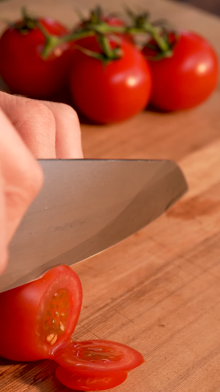 Slow-motion close-up of a fresh tomato being smoothly cut into even slices with a razor-sharp knife. The vibrant red texture and precise blade movement create a clean, detailed kitchen scene