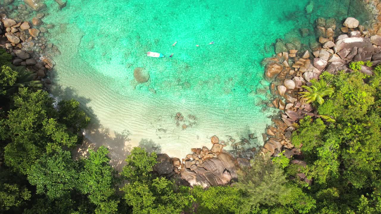 drone de la playa de anse major, vista de pájaro de 4 turistas buceando cerca del barco, piedras de granito, agua turquesa y playa de arena blanca, mahe seychelles 30 fps