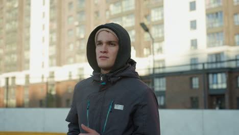 young man jogging on outdoor sport arena with focused expression, showcasing determination, fitness, and energy against residential building backdrop