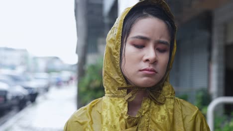 pretty asian girl wear yellow hoodie raincoat stuck in the rain , disappointment in pouring rain, rainy season weather, feeling down sad and lonely, bad stormy sorrow unhappy face  expression