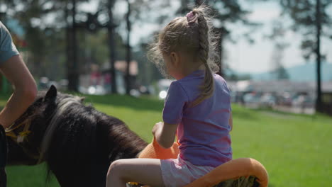 Little-child-rides-pony-with-instructor-along-city-garden