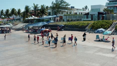 Truck-left-aerial-drone-shot-of-a-marching-band-and-teens-dressed-as-furry-bears-performing-and-asking-for-money-for-Carnaval-on-the-tropical-Bessa-beach-in-Joao-Pessoa,-Paraiba,-Brazil-on-summer-day