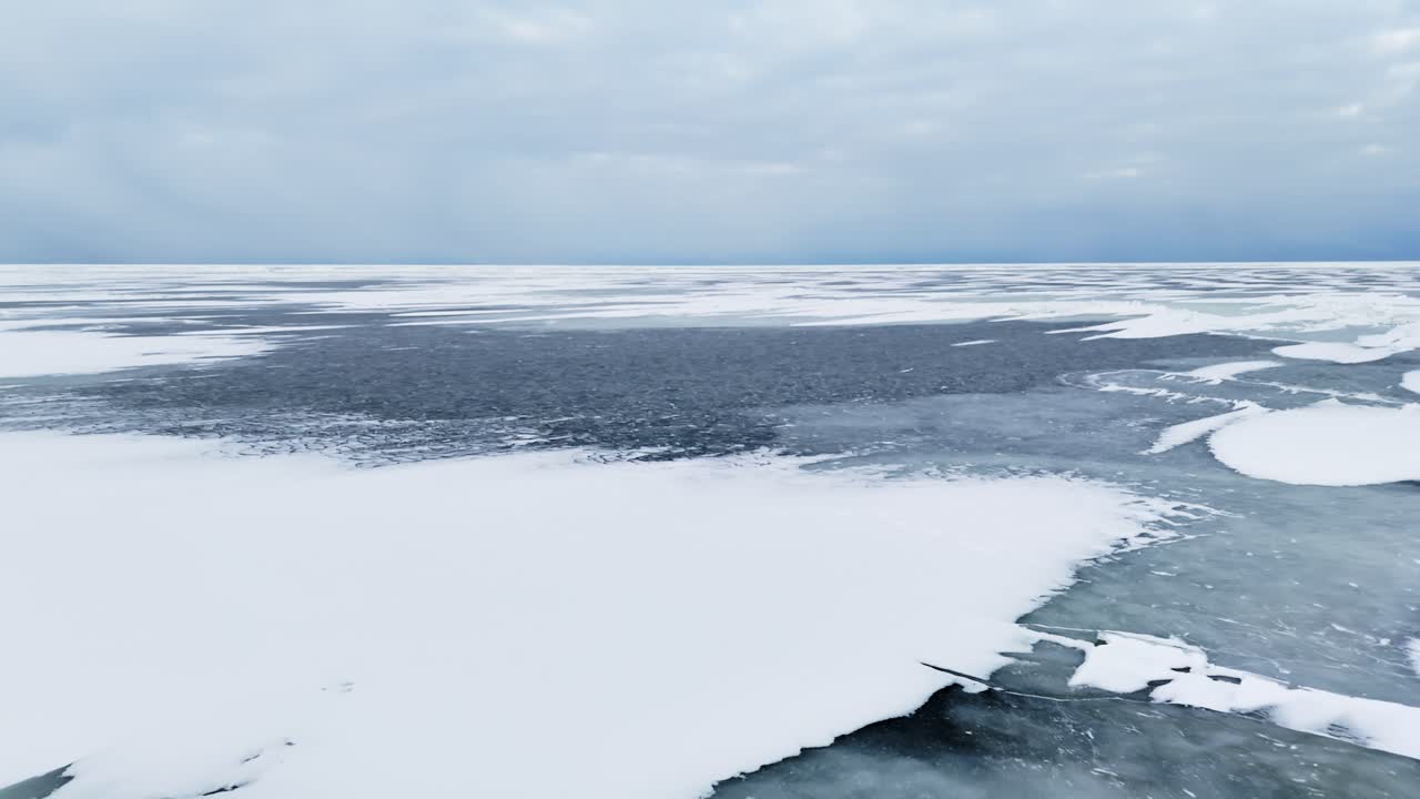 Scatto aereo verticale di ghiaccio marino del Baltico crepato con canali aperti scuri e creste di pressione sotto un cielo coperto, creando uno sfondo invernale freddo, minimale e potenzialmente pericoloso.