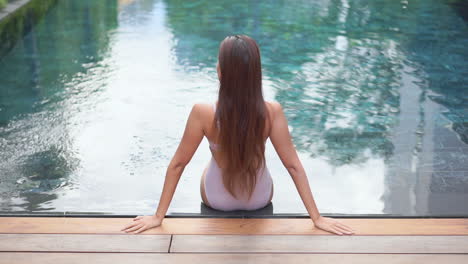 a woman sits on the edge of a swimming pool