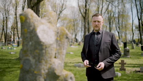 man in black suit in front a tombstone in a graveyard