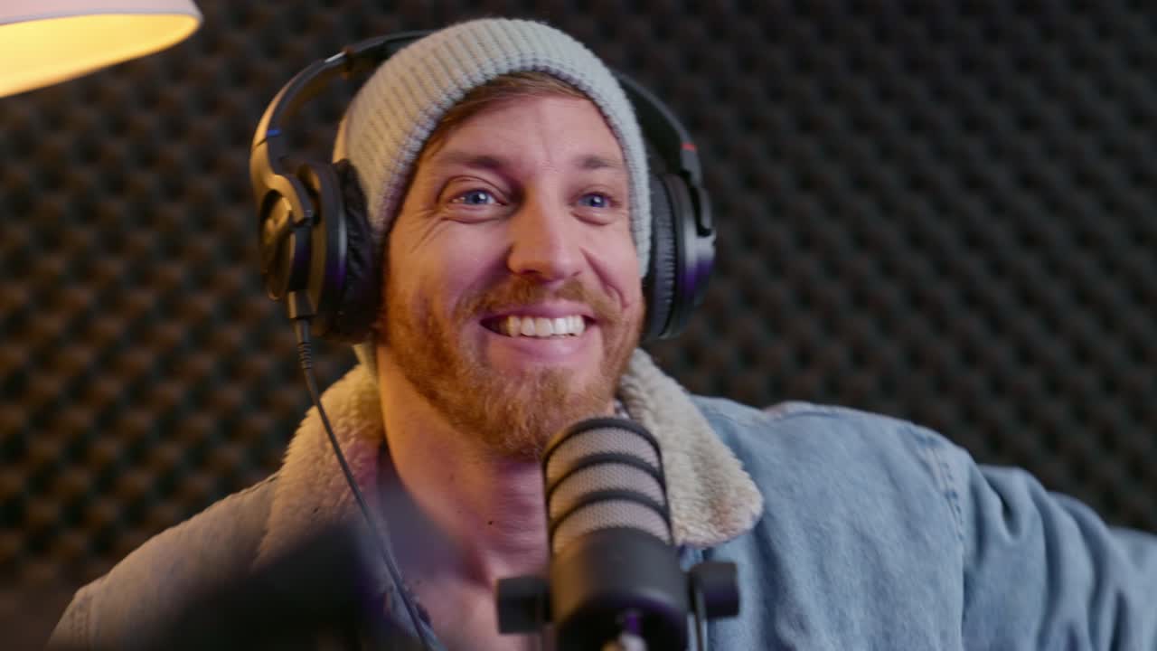 Hipster podcast or radio host setting up equipment and audio gear in studio. Professional sound proof booth with mic. Live streaming as man excited and happy getting ready to start a recording session