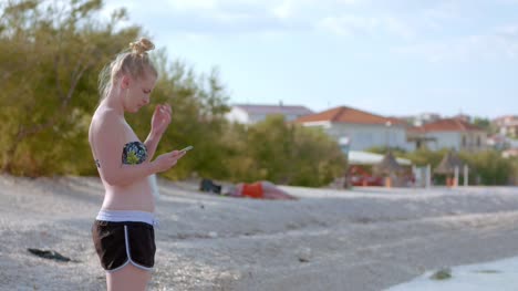 Junge-Dame-Sitzt-Am-Strand,-Während-Sie-Ihr-Mobilgerät-Benutzt-3-Using