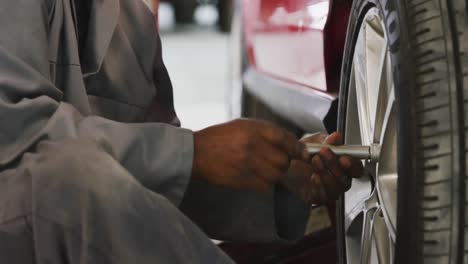 mecánico de automóviles afroamericano atornillando una rueda a un automóvil con una llave inglesa