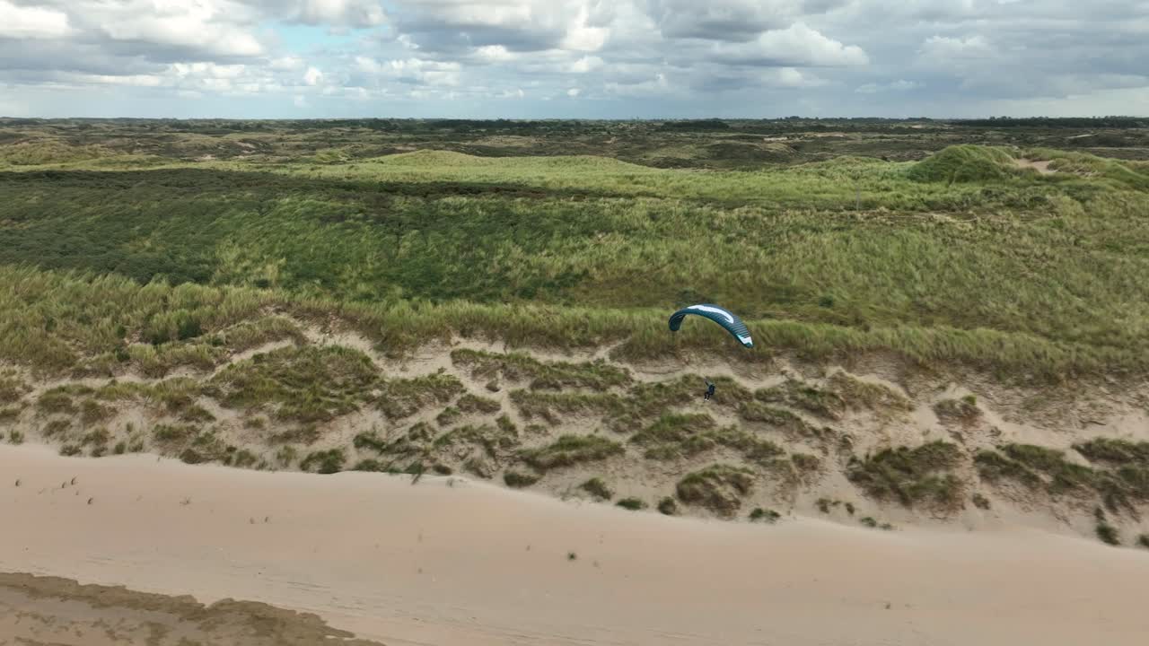 un dron aéreo de alta velocidad disparó a una persona que descendía en parapente por una playa en un día soleado en holanda