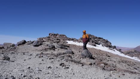 hombre camina por el sendero de la cumbre de la montaña más allá de la mancha de nieve contra el cielo azul