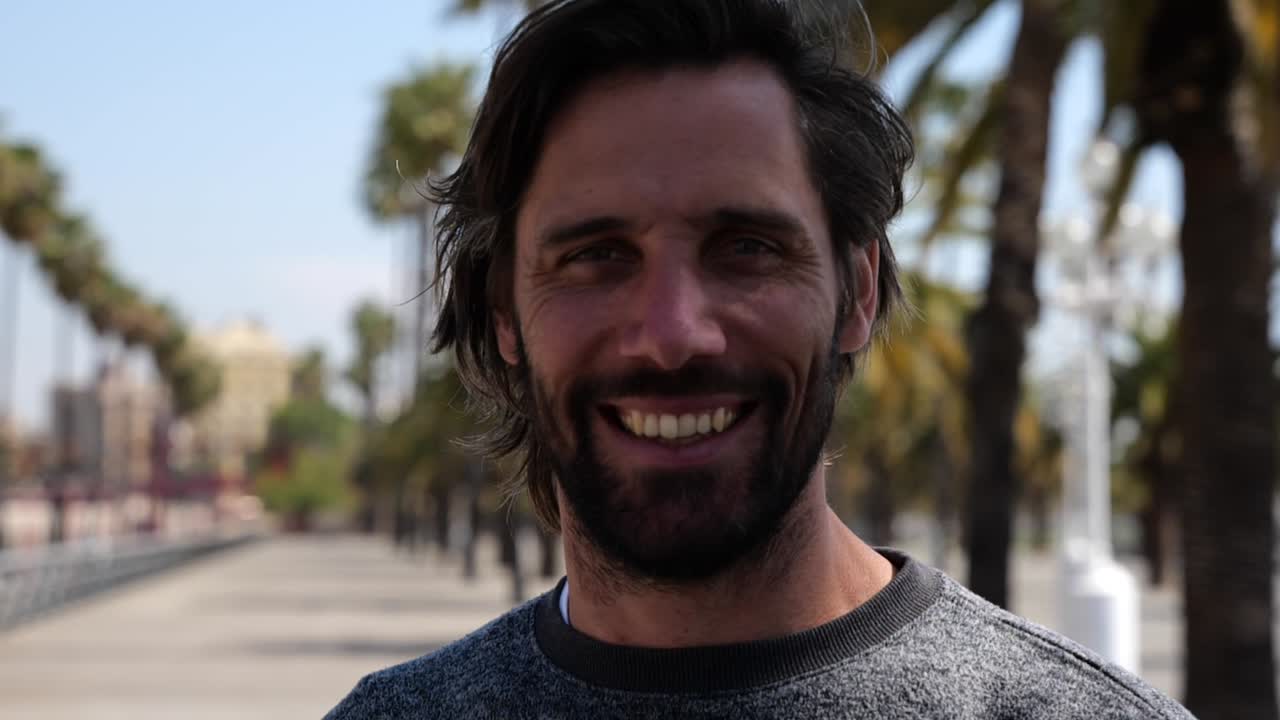 retrato de un apuesto hombre barbudo sonriendo con el paseo marítimo de barcelona en segundo plano