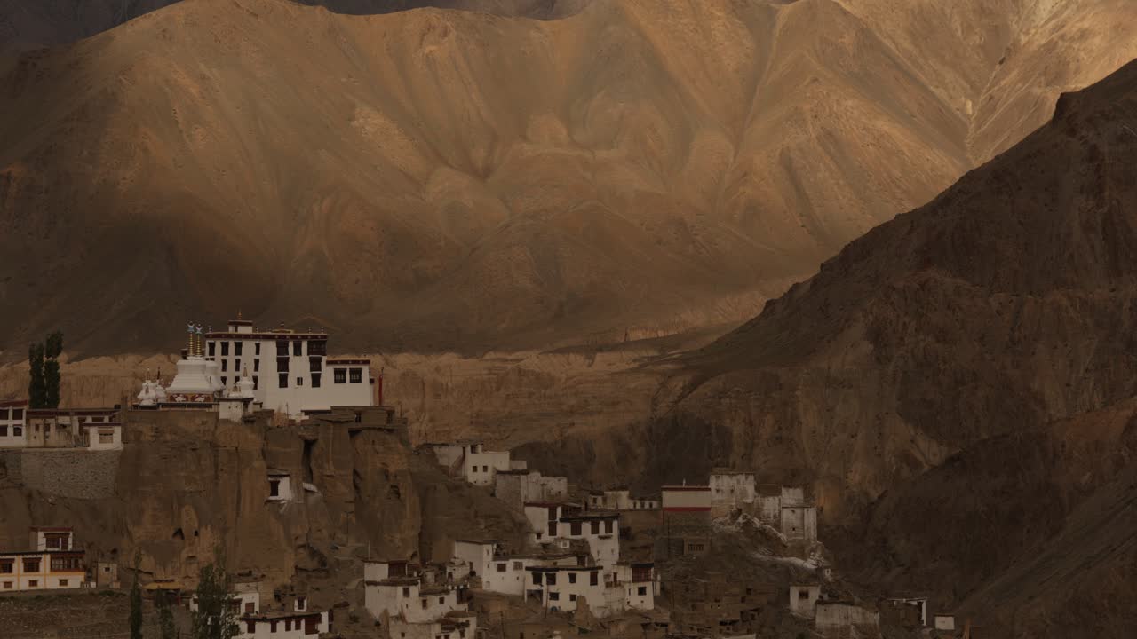 Gompa nestled on cliff with dramatic mountainous landscape, Timelapse with moving shadow and light from dynamic clouds. Copy space