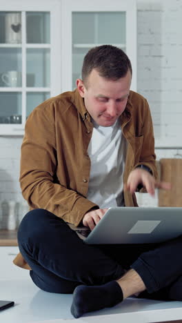 young man pressing buttons on a laptop at home. funny face of a businessman after working long hours on a computer. tired mad man on the table at home with a laptop. vertical video