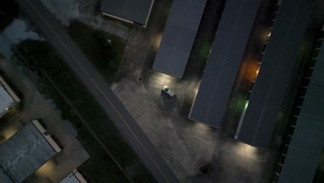 slowly descending drone shot of car parked near rows of metal roofed buildings in late afternoon