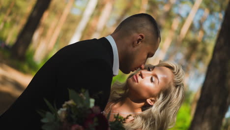 careful gentleman kisses cheek of beloved wife in forest