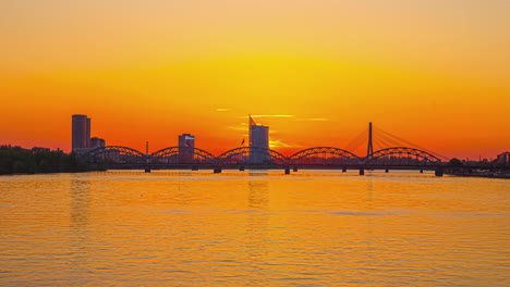 sunset over a river with the silhouette of bridges and city skyline in the background - time lapse