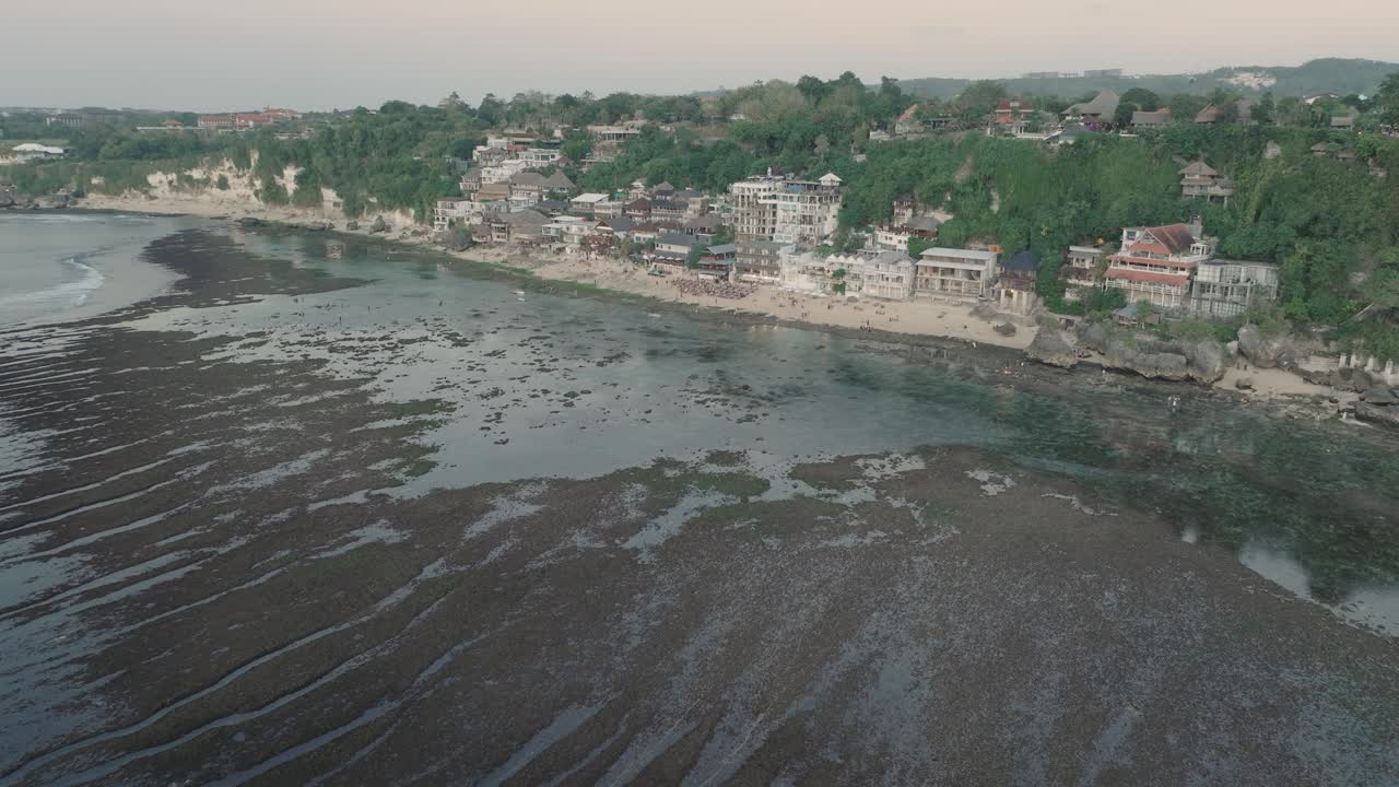 en la lejanía, una fotografía de aviones no tripulados de los edificios de la playa de bingin al atardecer y la marea baja en uluwatu bali, indonesia