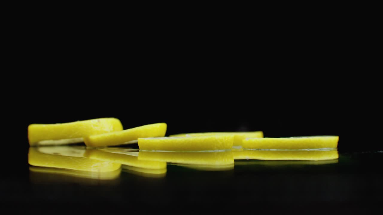 느린 동작: 슬라이스 된 레몬 반지는 어두운 배경에서 유리 위에 물 어리와 함께 떨어집니다.