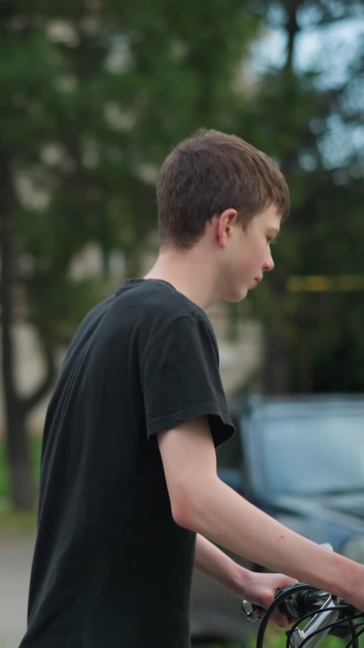 두 형제는 자전거를 고 나란히 고 있으며, 회색 을 입은 사람은 안경을 조정하고 다른 사람은 검은 을 착용하고 앞을 걸어가고 있으며, 배경에는 나무와 자동차의 부분적인 시각이 있습니다.