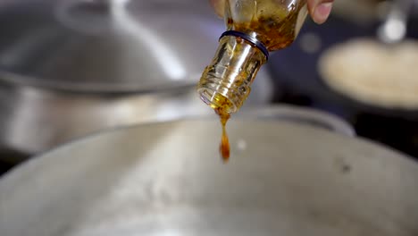 Chef-pours-chilli-garlic-sauce-flavours-into-spicy-Indian-cuisine-SLOW-MOTION,-CLOSE-UP