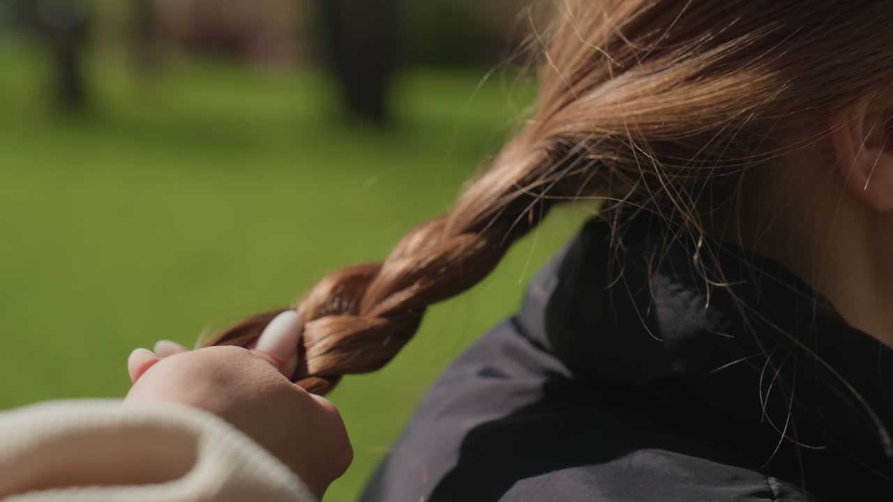 tutorial relajado de trenzado, sesión de trenzado de cabello cuidadosa llevada a cabo durante horas de luz solar tranquila, dedos hábiles elaboran meticulosamente una trenza lateral elegante en medio de un ambiente al aire libre diurno brillante
