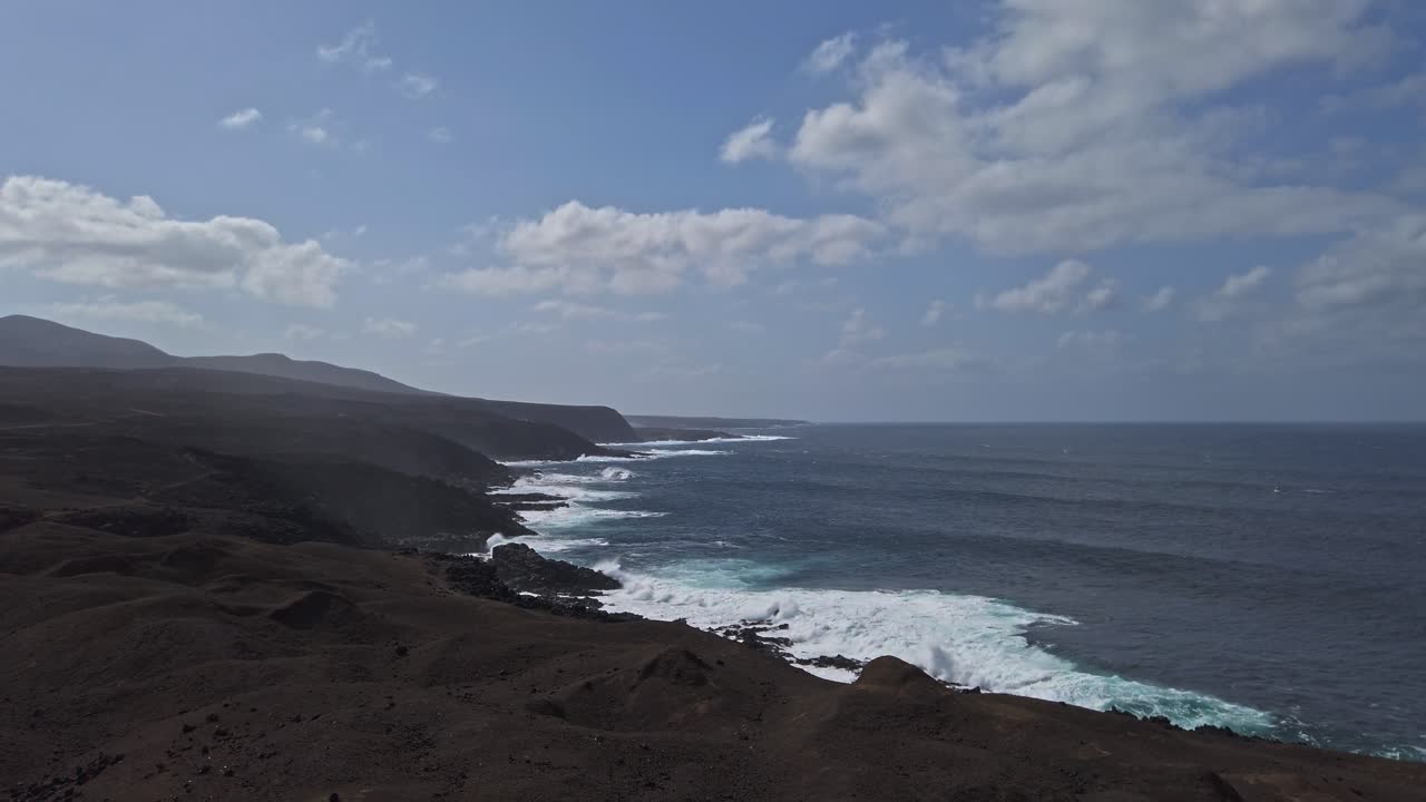 Volcanic black rocky coastline of lanzarote island in the canary islands, spain, meets the deep blue waters of the atlantic ocean under a bright blue sky dotted with white clouds